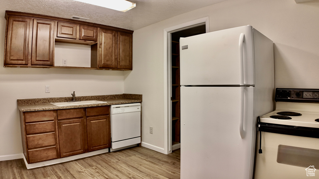 Kitchen with visible vents, white appliances, baseboards, a sink, and light wood finished floors