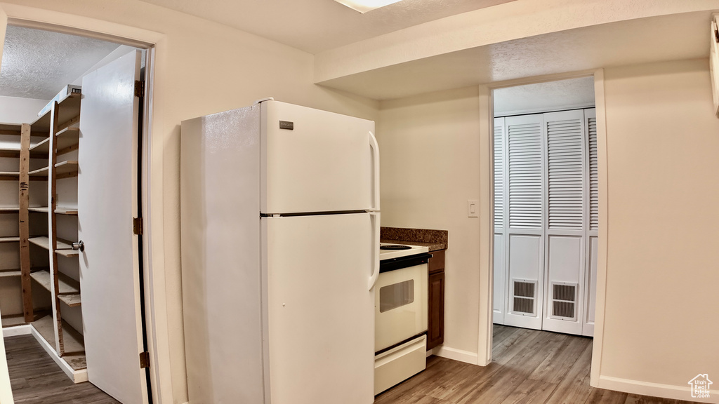 Kitchen featuring a textured ceiling, dark countertops, light wood-type flooring, baseboards, and white appliances