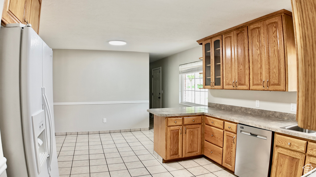 Kitchen featuring white fridge with ice dispenser, a peninsula, light tile patterned floors, stainless steel dishwasher, and glass insert cabinets