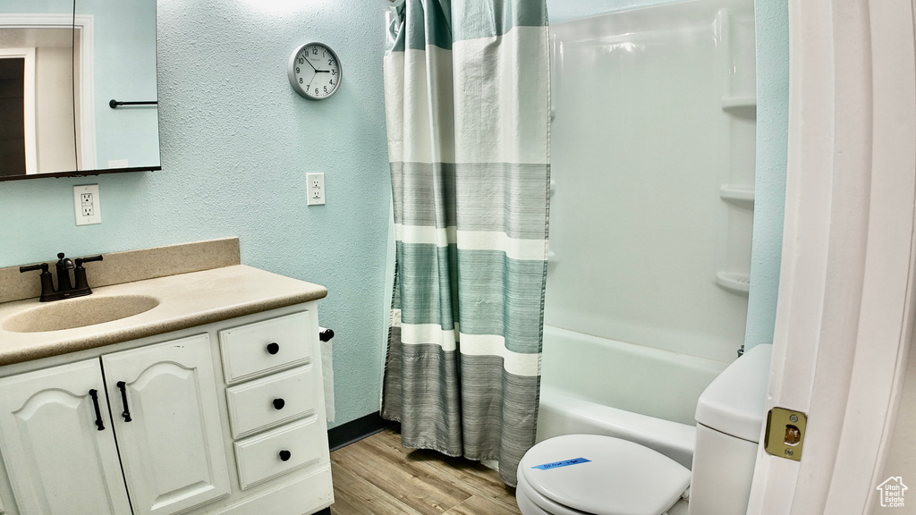 Full bath with a textured wall, vanity, toilet, shower / bath combo with shower curtain, and wood finished floors