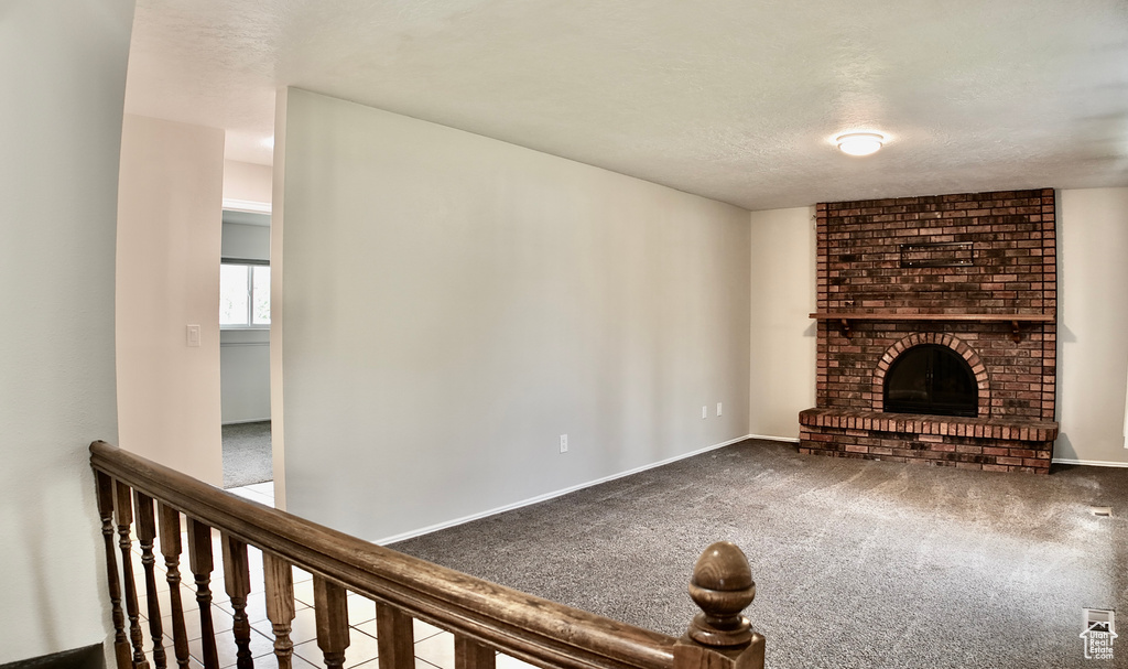 Unfurnished living room with carpet floors, a textured ceiling, baseboards, and a fireplace