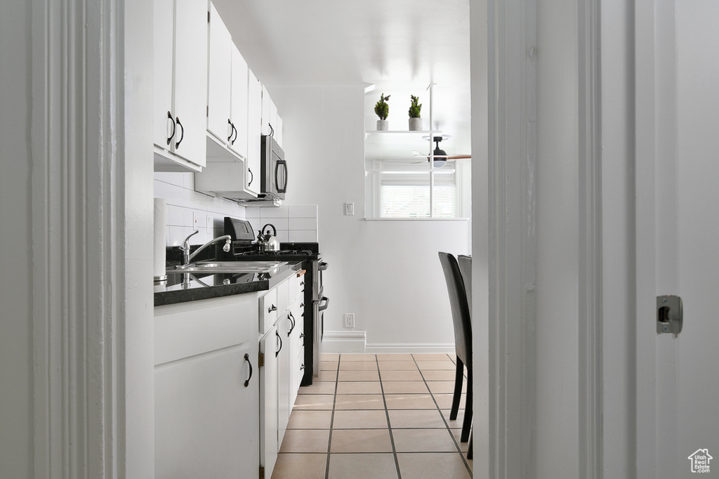 Kitchen featuring white cabinets, dark countertops, appliances with stainless steel finishes, light tile patterned floors, and tasteful backsplash