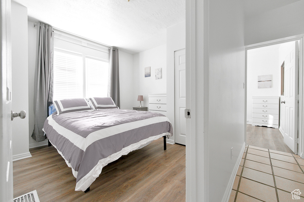 Bedroom featuring light wood-style floors, baseboards, a textured ceiling, and visible vents