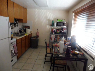 Kitchen featuring light tile patterned flooring, stove, brown cabinetry, freestanding refrigerator, and stainless steel microwave
