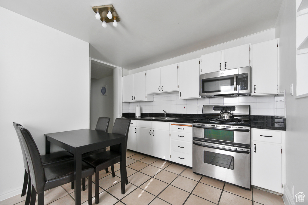 Kitchen with appliances with stainless steel finishes, tasteful backsplash, dark countertops, a sink, and white cabinetry