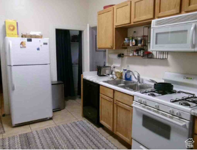 Kitchen with light tile patterned floors, light countertops, white appliances, and a sink