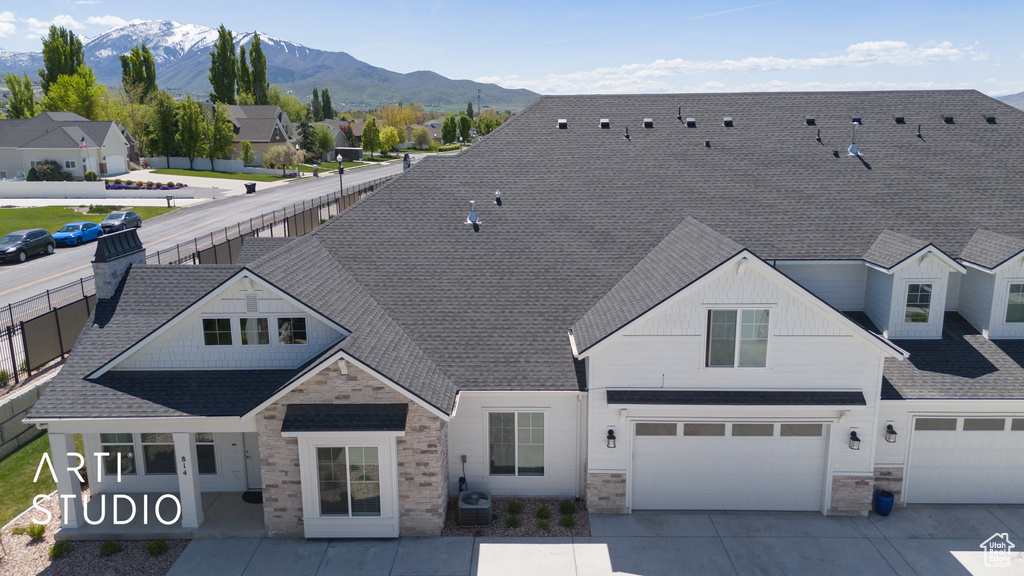 View of front of house featuring a mountain view, an attached garage, concrete driveway, stone siding, and roof with shingles