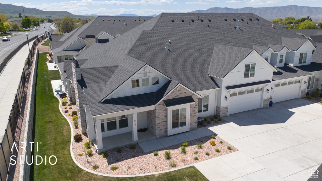 View of front of property with stone siding, a mountain view, fence, a shingled roof, and driveway