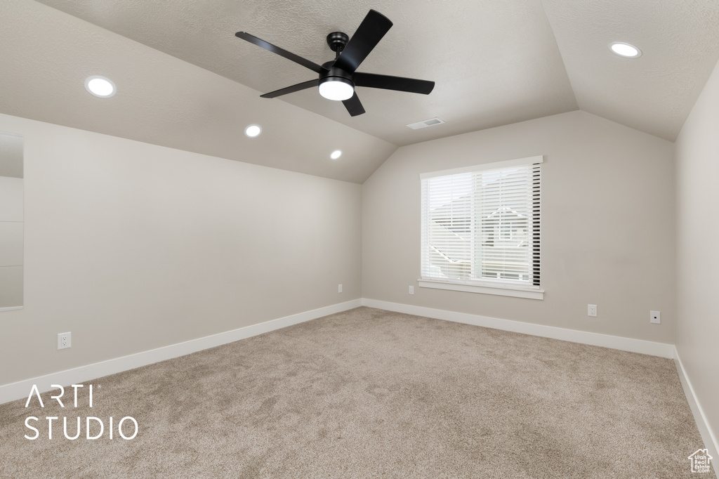 Empty room with ceiling fan, lofted ceiling, carpet flooring, and visible vents