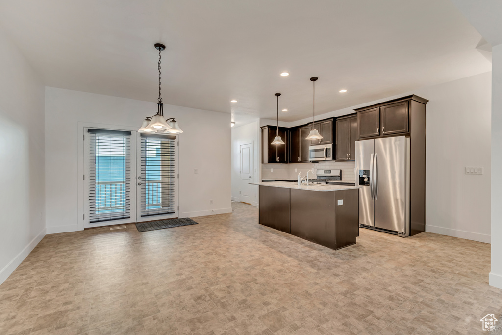 Kitchen with light countertops, dark brown cabinets, baseboards, a center island with sink, and stainless steel appliances