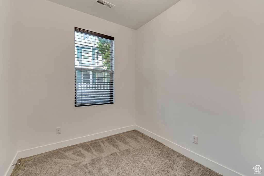 Empty room featuring vaulted ceiling, light colored carpet, baseboards, and visible vents