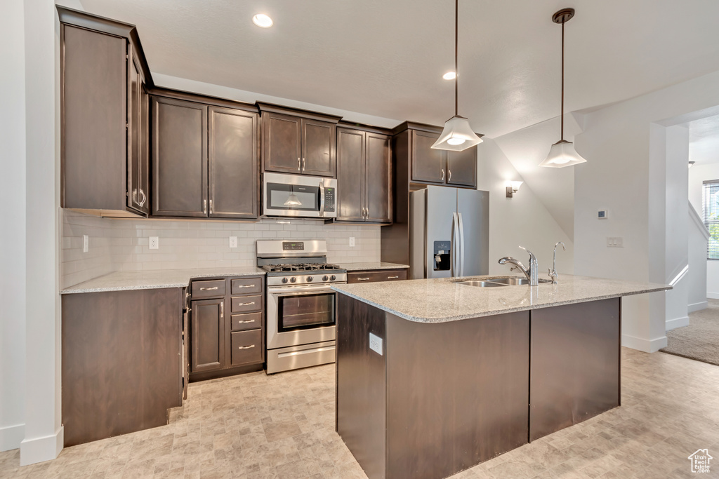 Kitchen with a sink, stainless steel appliances, decorative backsplash, light stone countertops, and dark brown cabinets