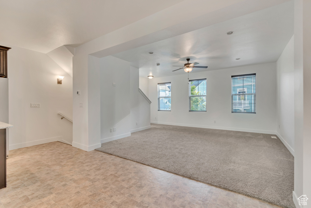 Unfurnished living room with light colored carpet, baseboards, and a ceiling fan