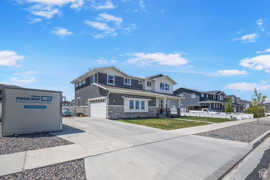 View of front facade with stone siding, an attached garage, fence, concrete driveway, and board and batten siding
