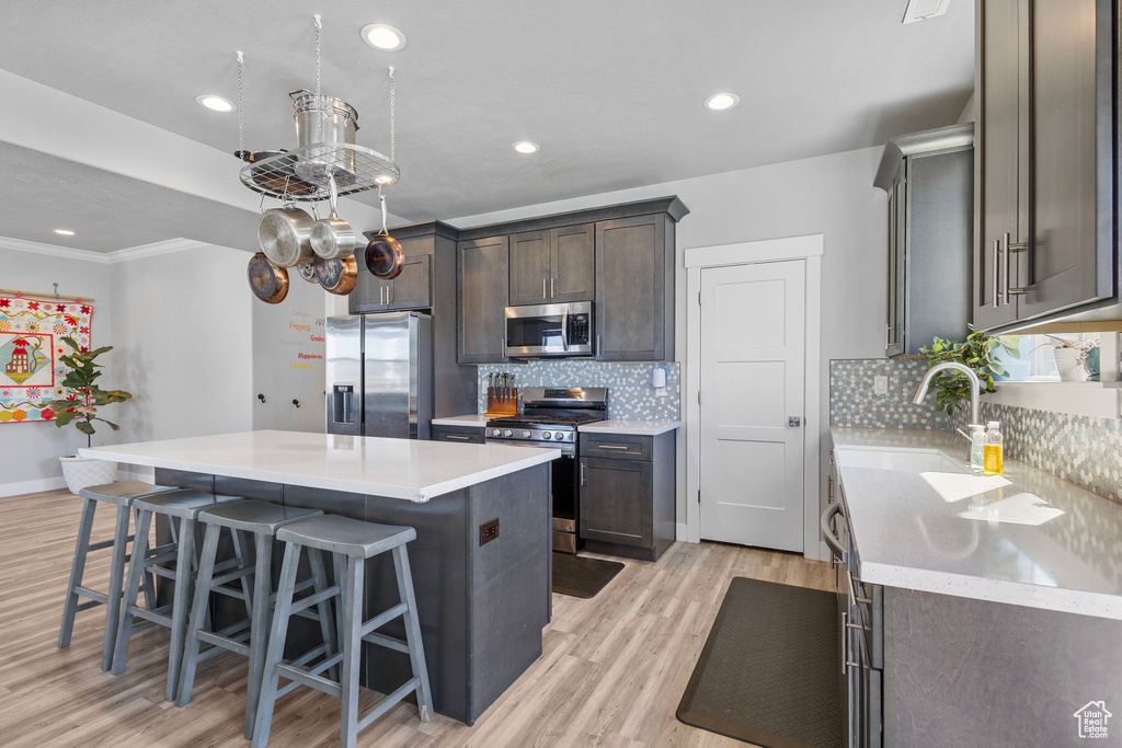 Kitchen featuring a sink, tasteful backsplash, light wood finished floors, a center island, and appliances with stainless steel finishes