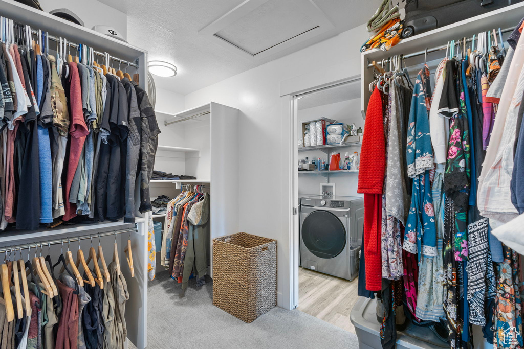Walk in closet featuring washing machine and clothes dryer, attic access, and wood finished floors