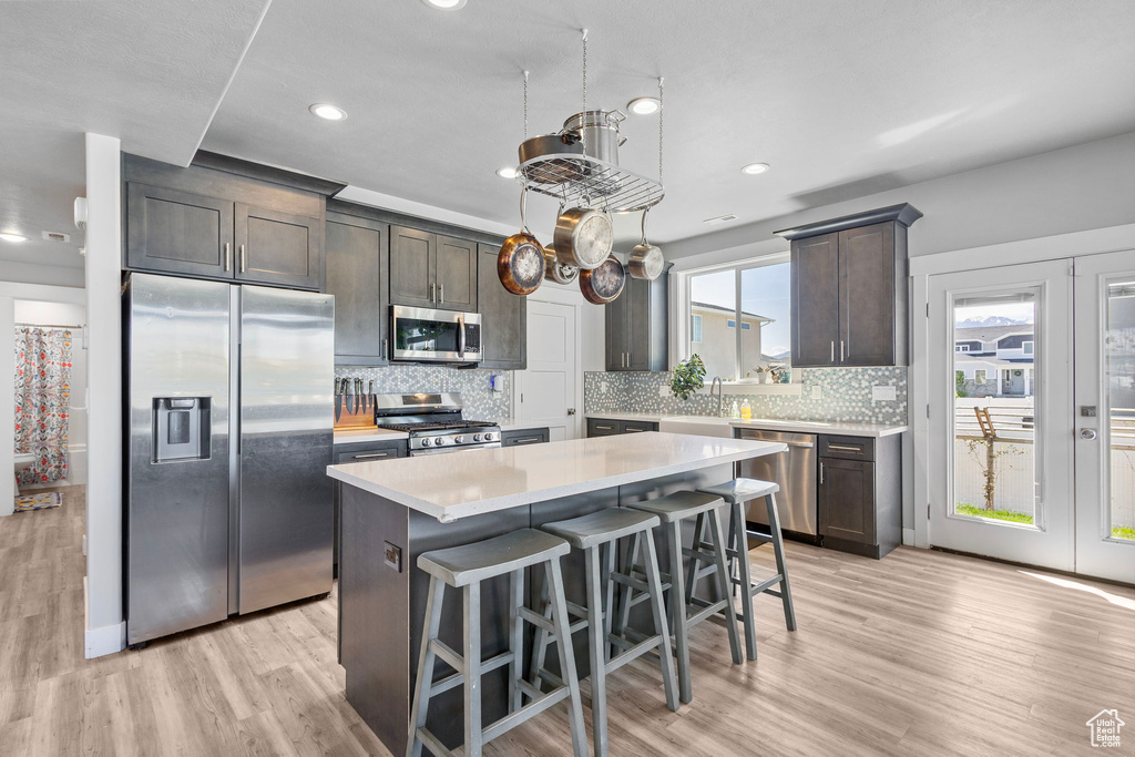 Kitchen with a breakfast bar area, light wood finished floors, dark brown cabinetry, light countertops, and appliances with stainless steel finishes