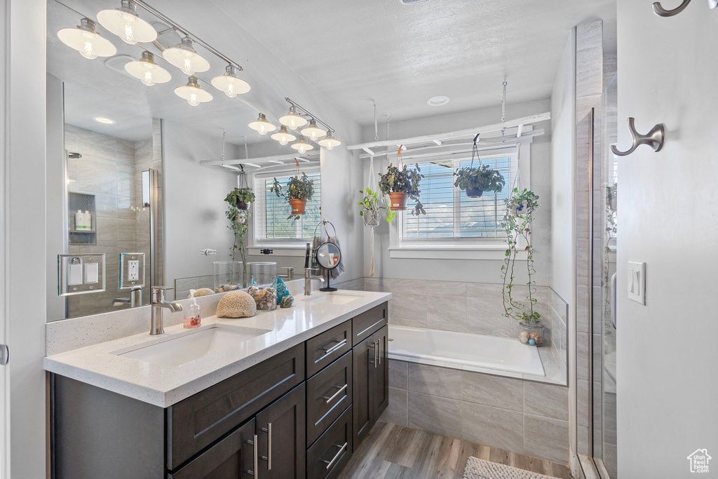 Full bathroom featuring double vanity, wood finished floors, tiled shower, a sink, and tiled tub