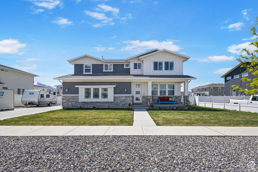 View of front of house with stone siding, fence, a front lawn, board and batten siding, and a porch