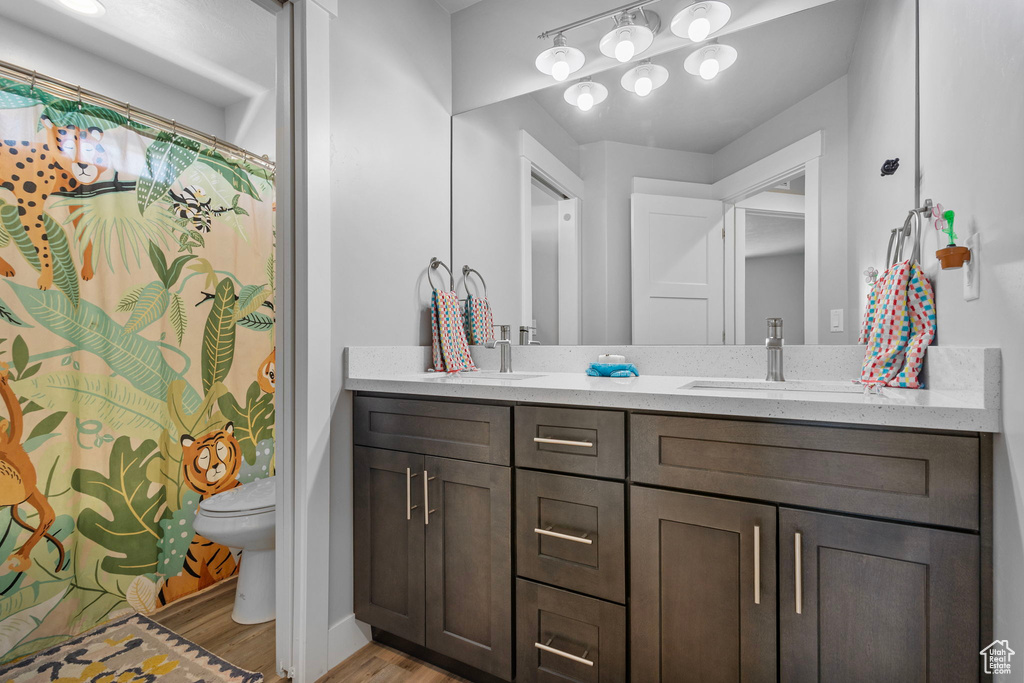 Bathroom with double vanity, toilet, wood finished floors, a sink, and baseboards