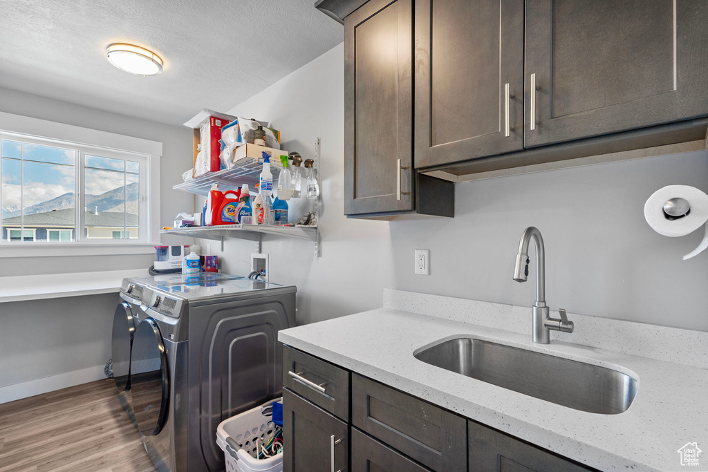 Laundry room with washing machine and clothes dryer, light wood-style flooring, cabinet space, and a sink
