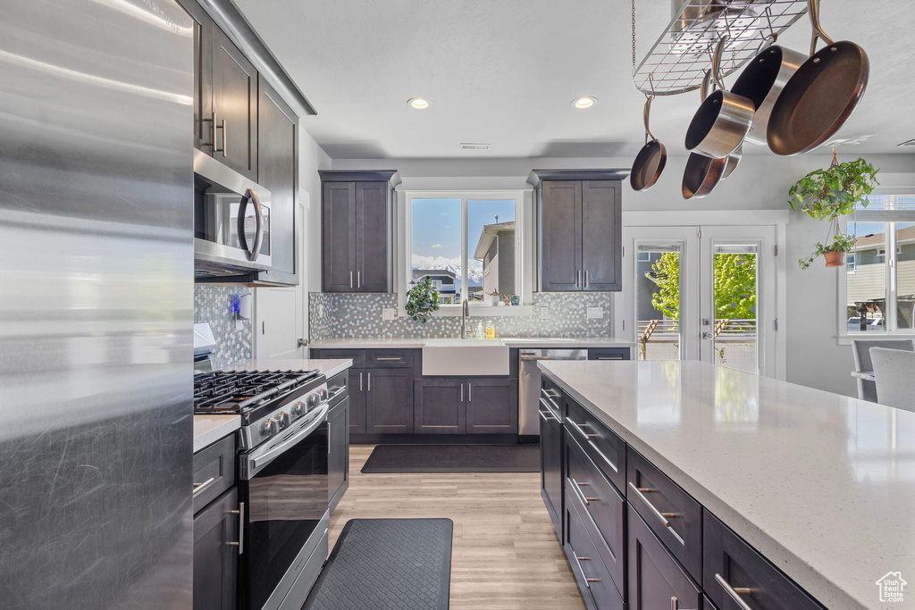 Kitchen with a sink, appliances with stainless steel finishes, light wood-style floors, tasteful backsplash, and recessed lighting