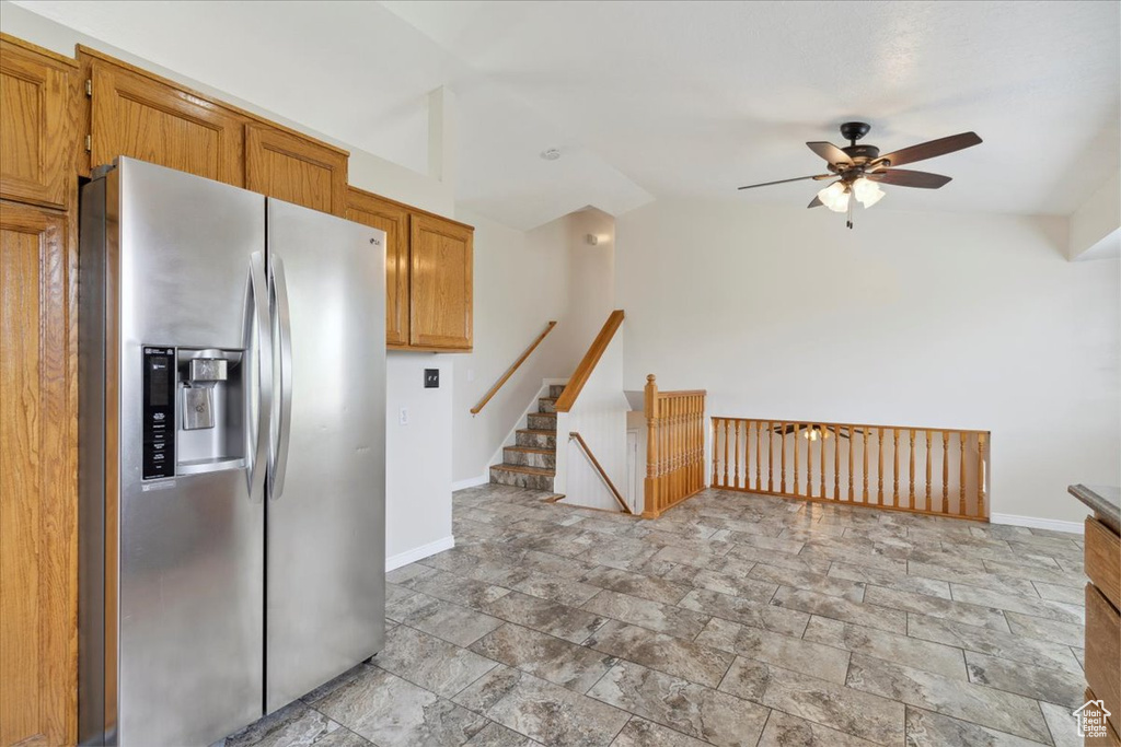 Kitchen with stone tile floors, baseboards, ceiling fan, stainless steel fridge, and brown cabinets
