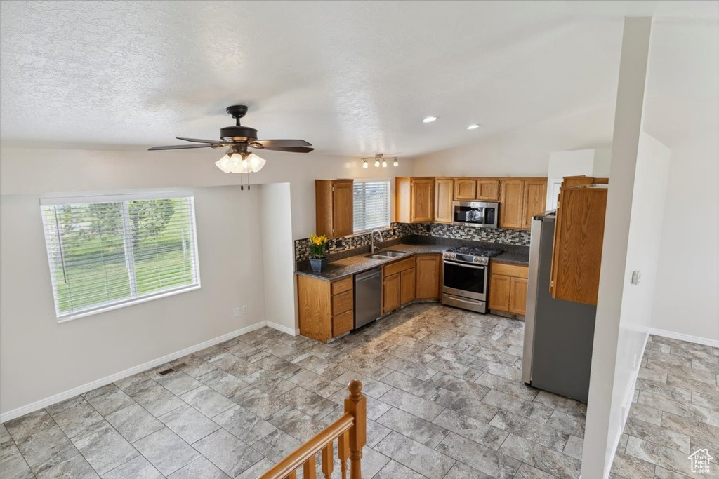 Kitchen featuring a sink, stainless steel appliances, a ceiling fan, baseboards, and dark countertops