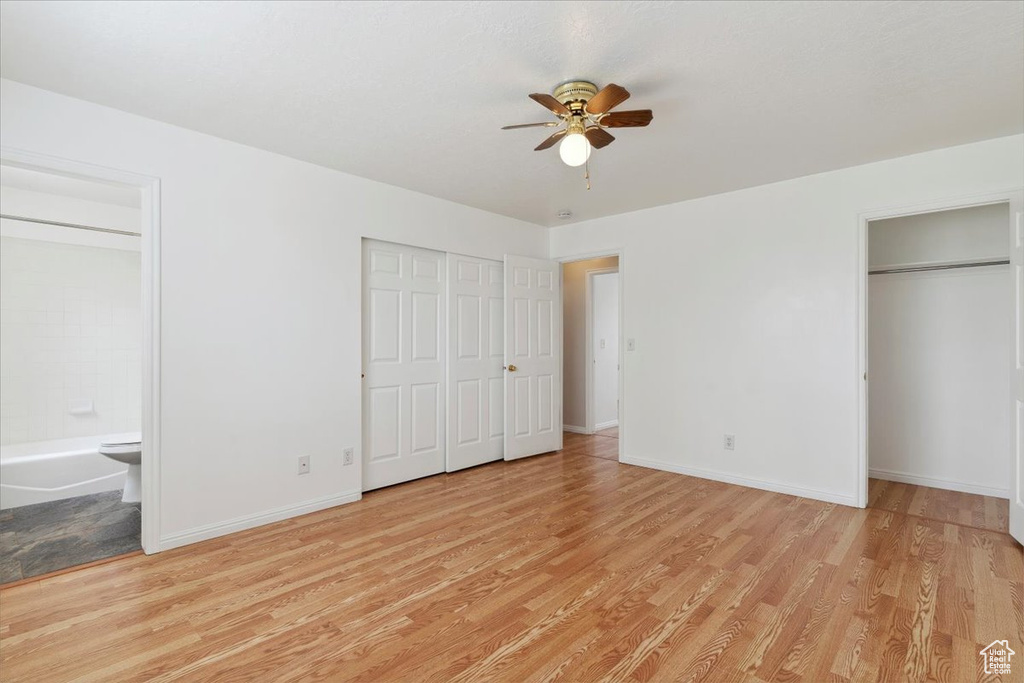 Unfurnished bedroom featuring a ceiling fan, multiple closets, ensuite bathroom, baseboards, and light wood-style floors