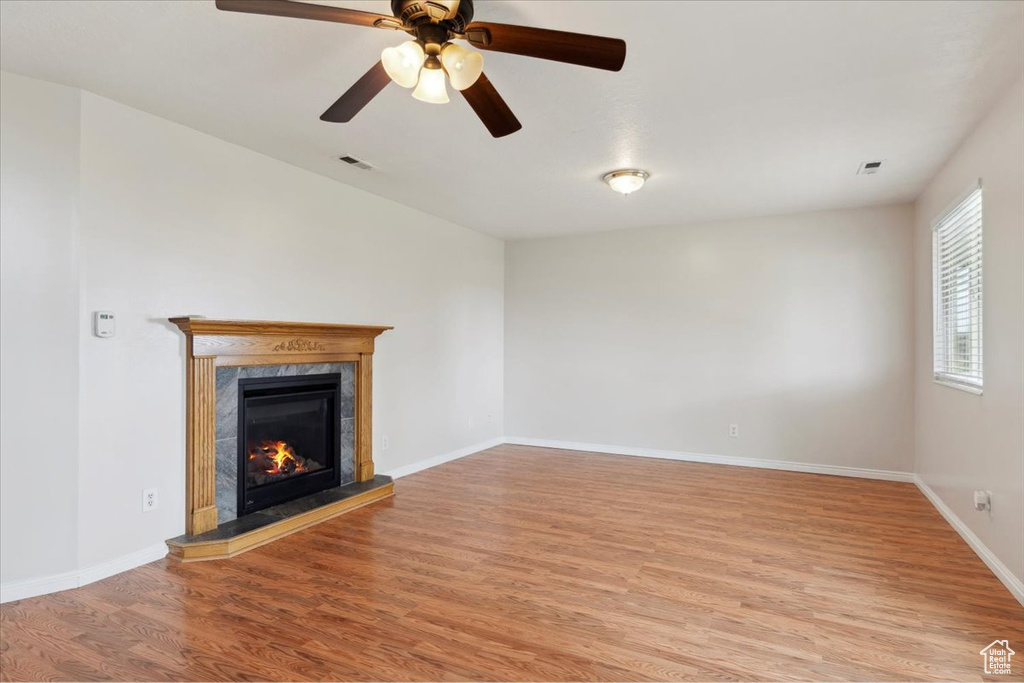 Unfurnished living room with a premium fireplace, baseboards, ceiling fan, visible vents, and light wood-type flooring
