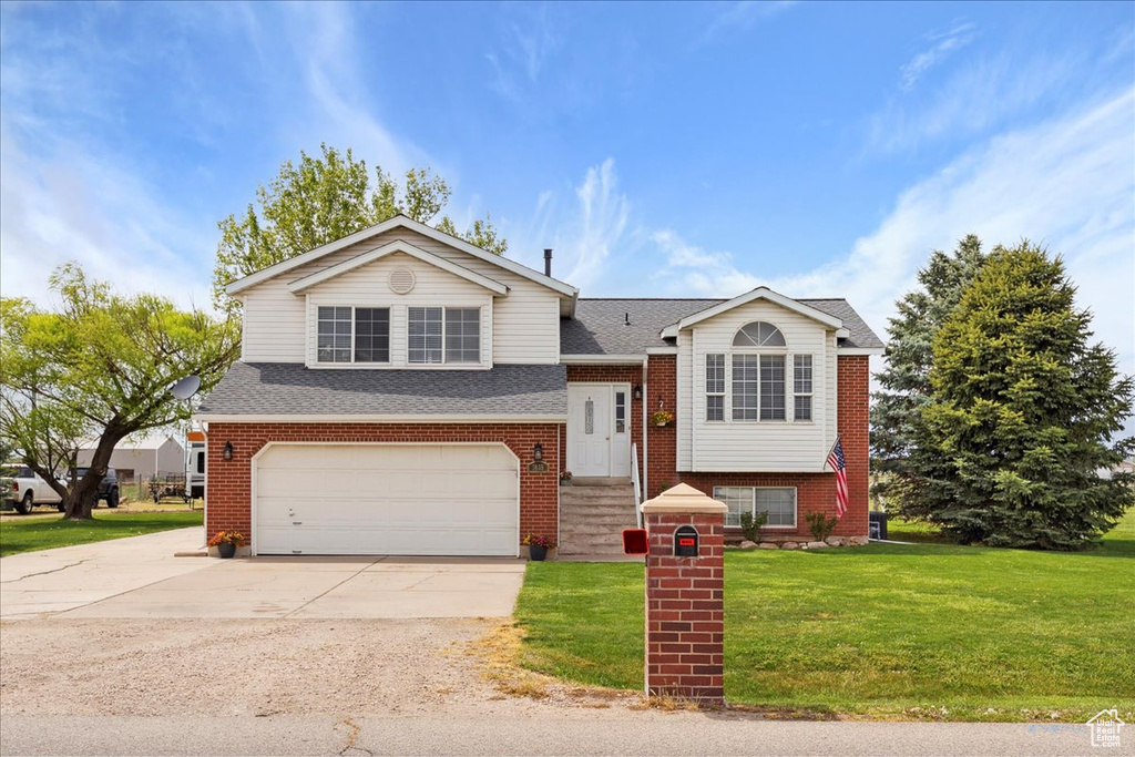 View of front of property featuring a garage, a shingled roof, brick siding, and a front yard