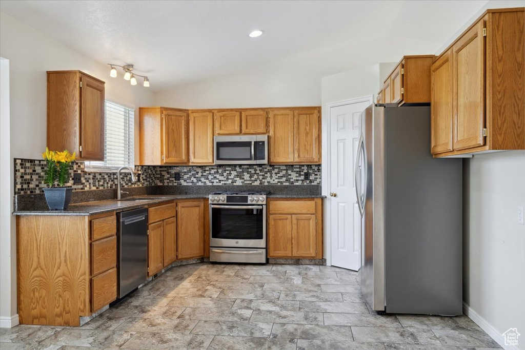 Kitchen with a sink, backsplash, dark countertops, and appliances with stainless steel finishes
