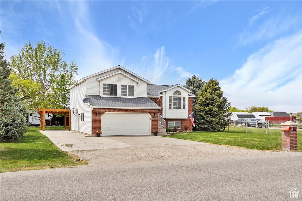 Tri-level home with brick siding, an attached garage, concrete driveway, a front yard, and roof with shingles