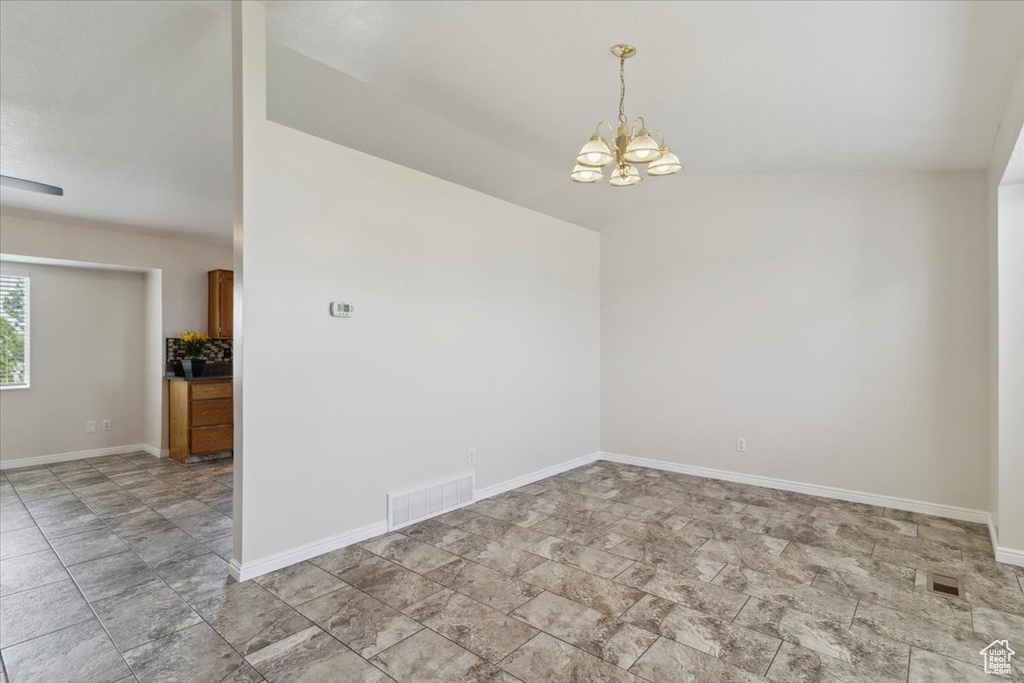 Empty room featuring baseboards, a notable chandelier, visible vents, and stone finish floor