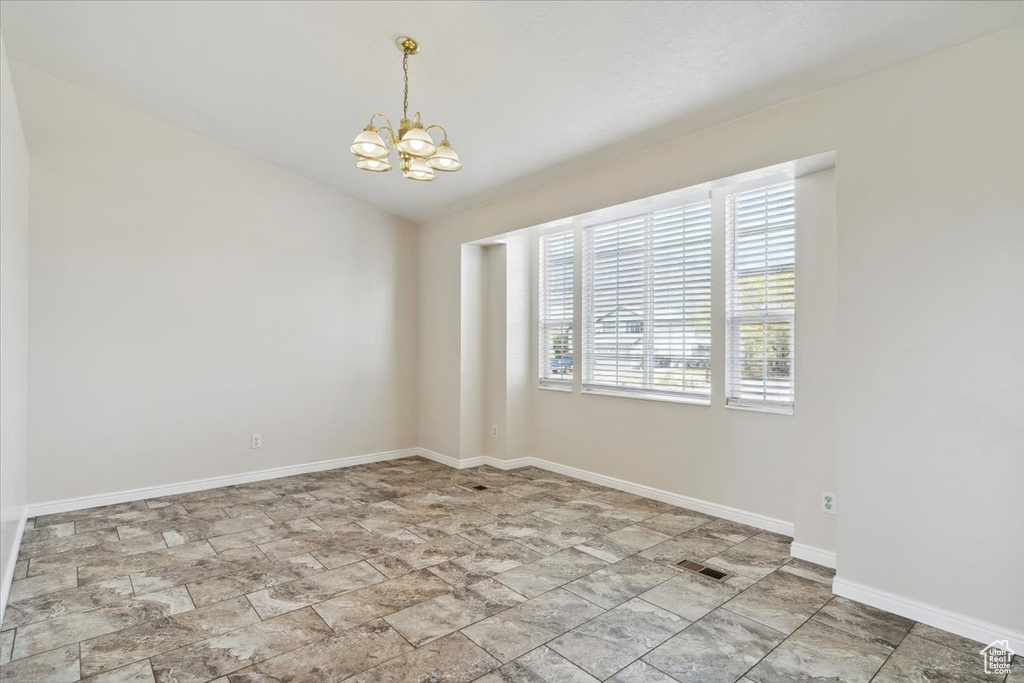 Spare room with lofted ceiling, a notable chandelier, baseboards, stone finish flooring, and visible vents