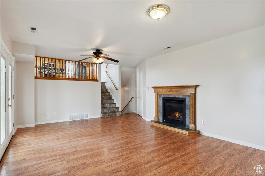 Unfurnished living room with a fireplace, ceiling fan, visible vents, and wood finished floors