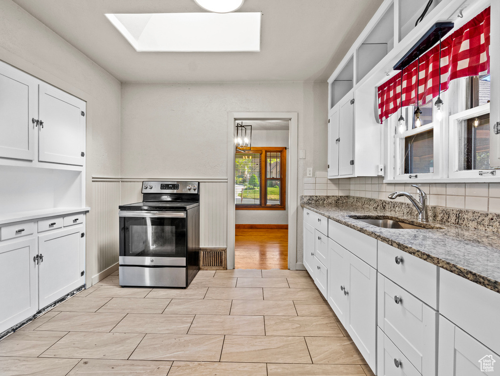 Kitchen with stainless steel range with electric stovetop, a skylight, a sink, white cabinets, and a wainscoted wall