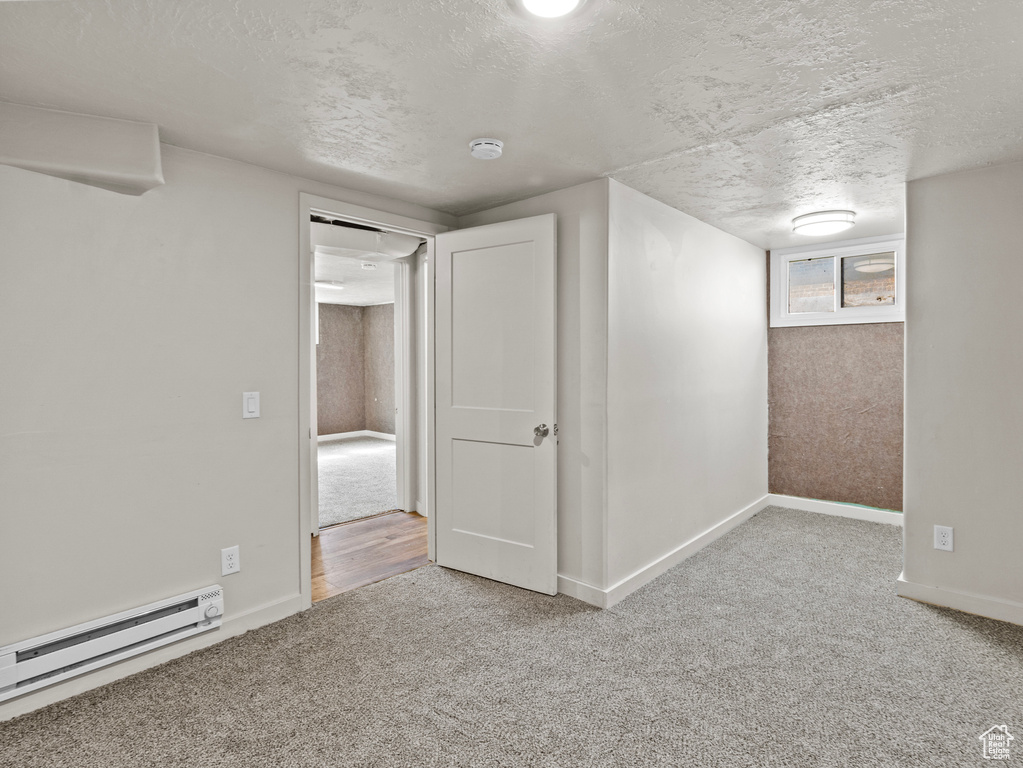 Below grade area with a baseboard radiator, a textured ceiling, carpet, and baseboards