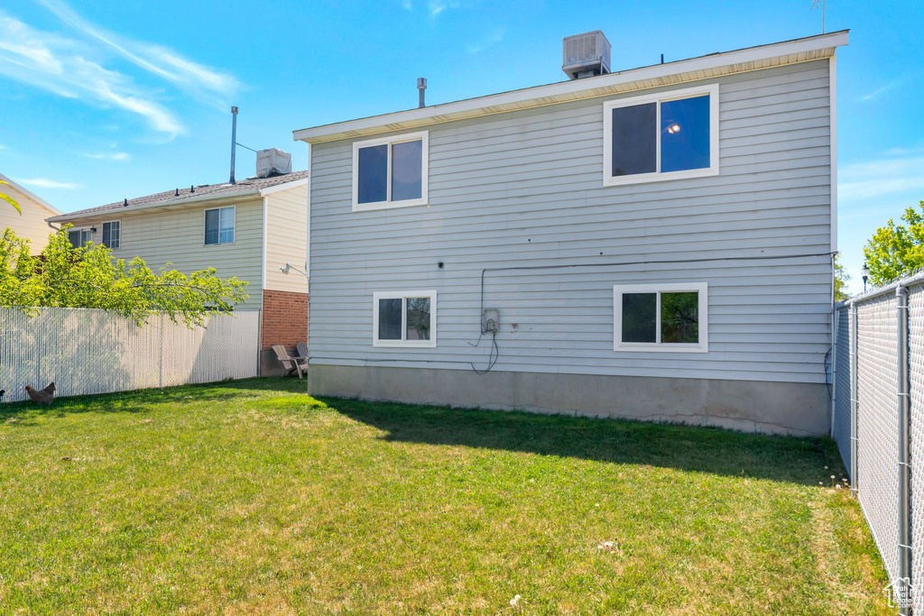 Back of property with cooling unit, a yard, and fence