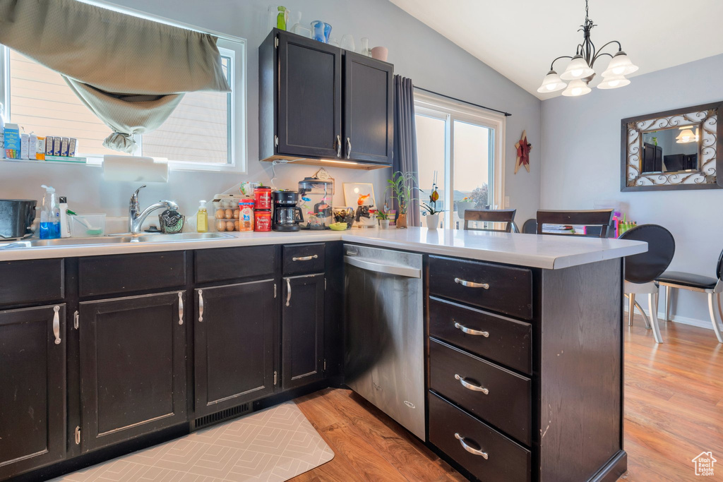 Kitchen featuring a sink, a peninsula, dishwasher, vaulted ceiling, and light wood-style flooring