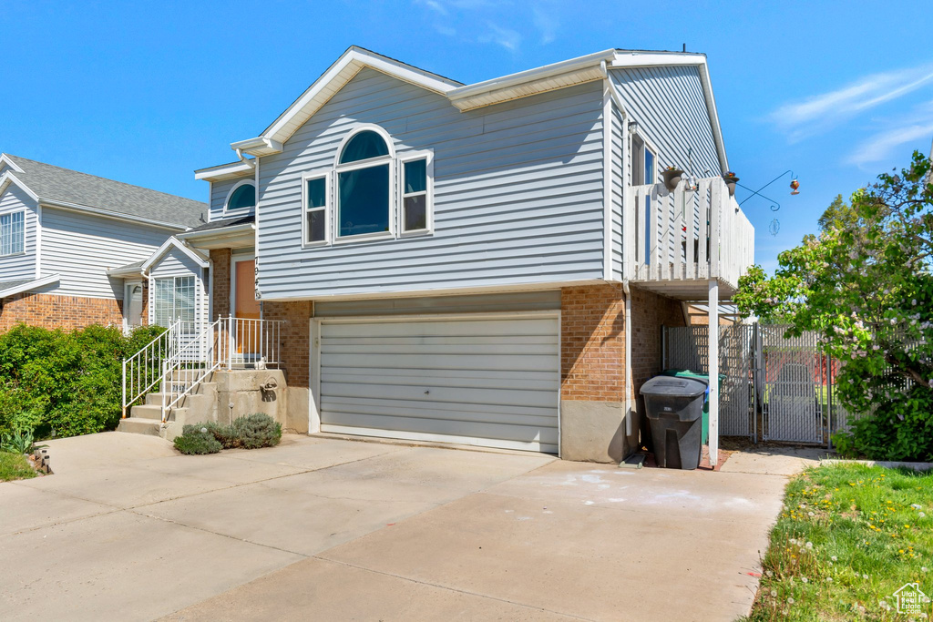 Tri-level home with a gate, an attached garage, brick siding, a balcony, and driveway