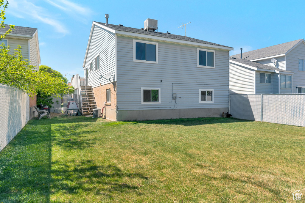 Rear view of property with cooling unit, a lawn, a fenced backyard, and stairs