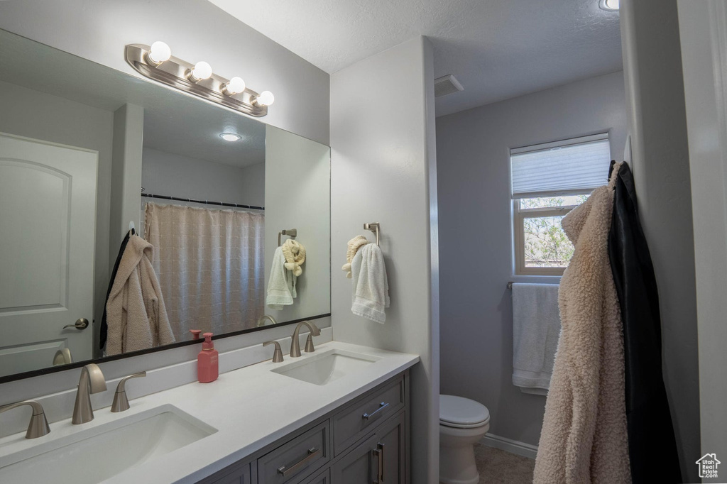 Bathroom featuring toilet, baseboards, double vanity, and a sink