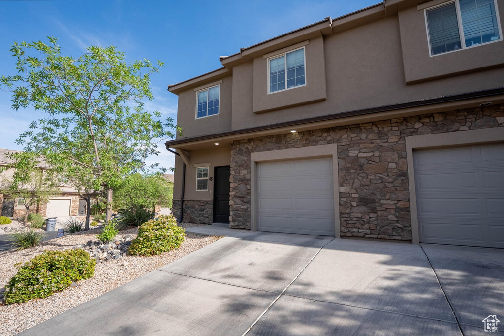 Multi unit property with concrete driveway, stone siding, stucco siding, and an attached garage