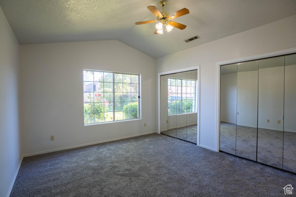 Unfurnished bedroom featuring baseboards, carpet flooring, visible vents, two closets, and vaulted ceiling