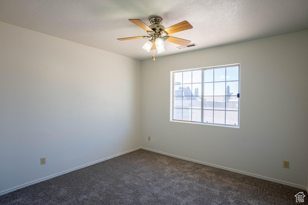 Carpeted empty room with baseboards, visible vents, and a ceiling fan
