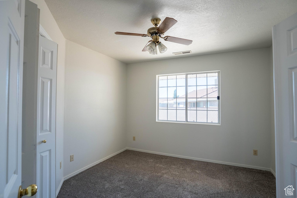Empty room with carpet, a textured ceiling, visible vents, baseboards, and ceiling fan