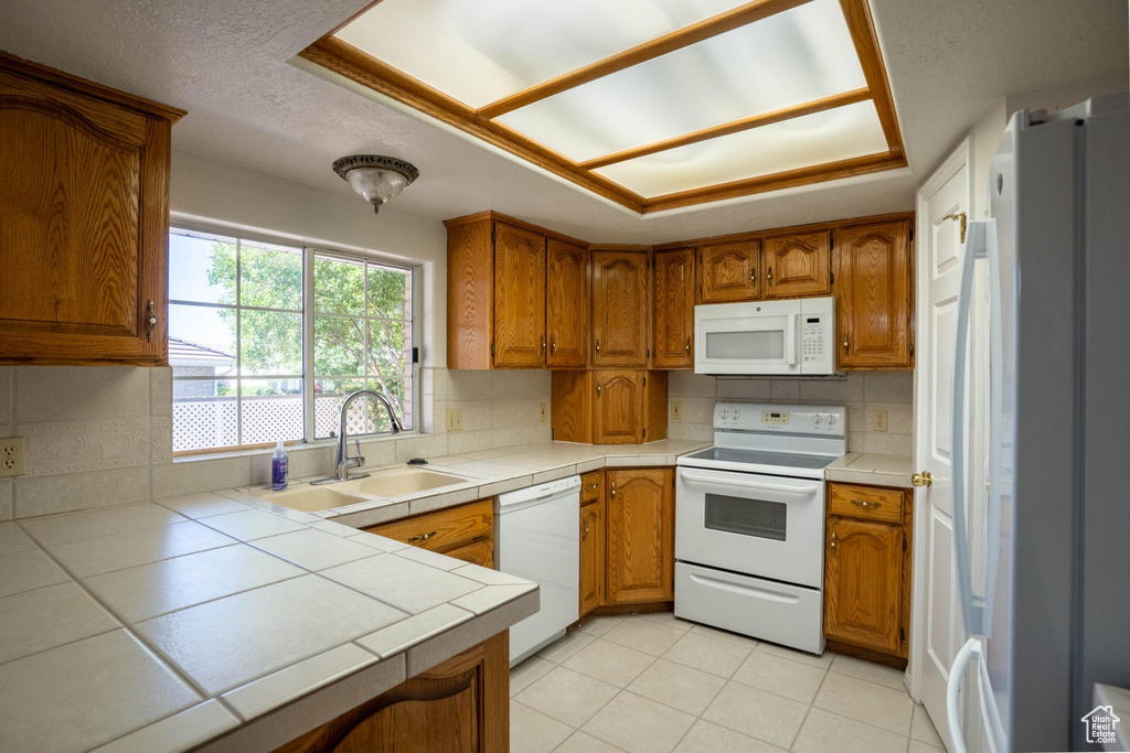 Kitchen with tile countertops, brown cabinetry, a sink, and white appliances