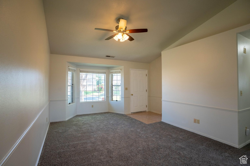 Carpeted spare room with a ceiling fan, baseboards, visible vents, and vaulted ceiling