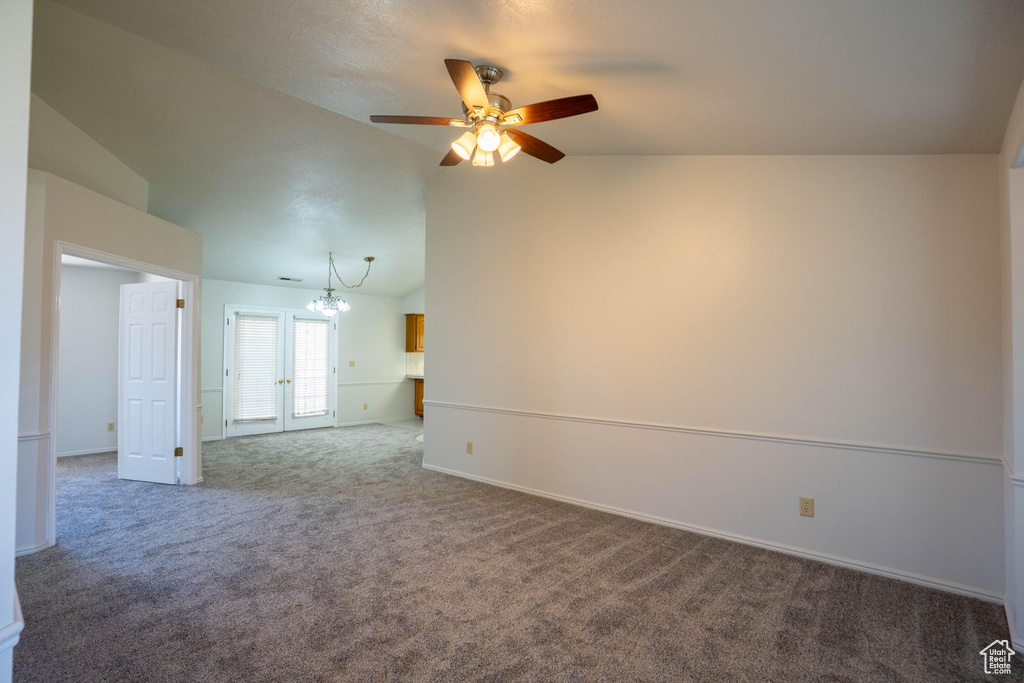 Carpeted spare room featuring vaulted ceiling, ceiling fan with notable chandelier, and baseboards